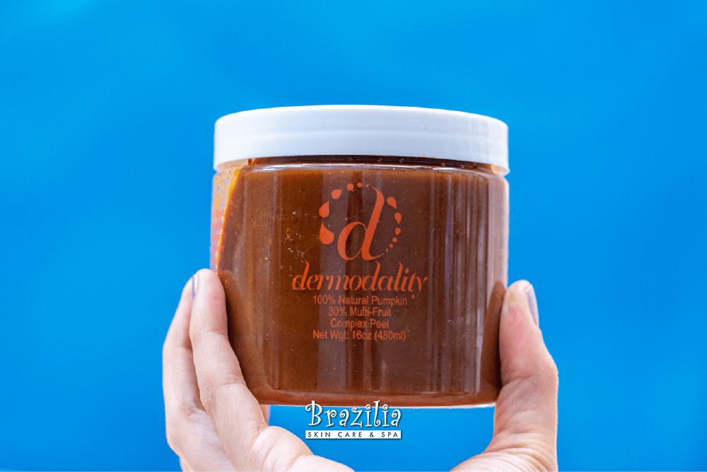 Hand holding a jar of Dermadality against a plain blue background