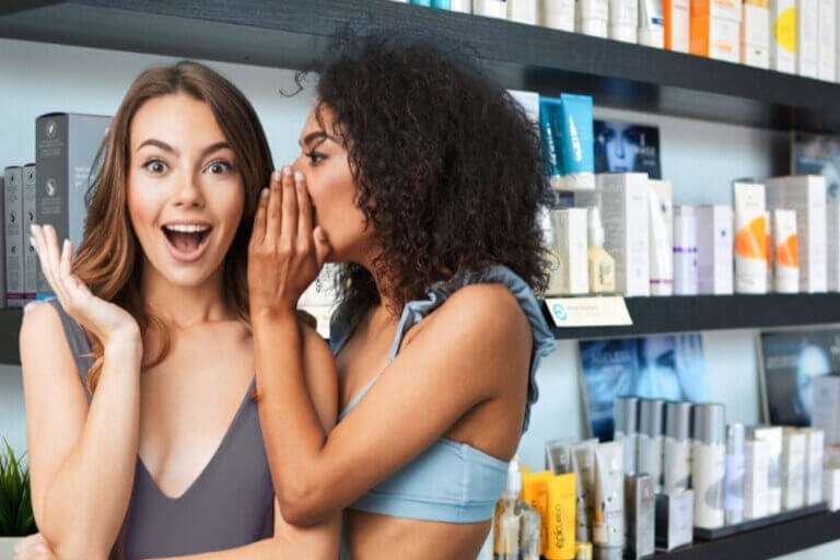 Woman tells another woman a secret, beauty products behind them